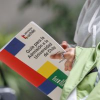 Se ven las manos y parte del torso de una postulante sosteniendo la publicación: Guía para la admisión a la Universidad de Chile