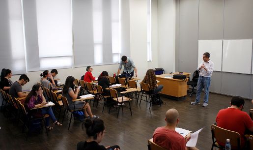 Sala de clases, con estudiantes sentadas y sentados, donde un profesor habla al frente.