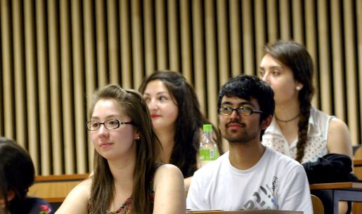 Medio plano de estudiantes, principalmente una mujer y un hombre, sentados en una sala de clases, mirando al frente.