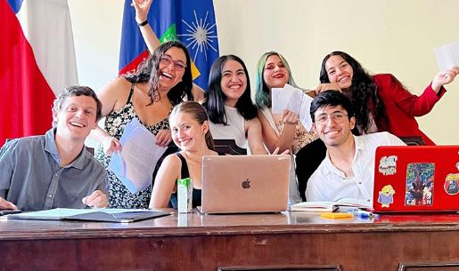 Grupo de siete estudiantes, posando con una sonrisa, con dos computadores al frente y las banderas de Chile y la Universidad de Chile, detrás