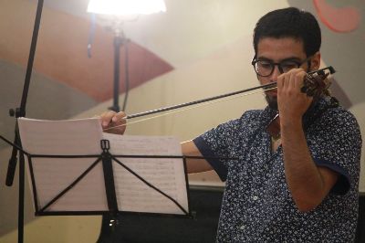 Plano medio de Nicolás González, estudiante de quinto año de Interpretación Musical de la Facultad de Artes de la Universidad de Chile y tutor integral par, tocando el violín en el Salón de Honor de Casa Central.