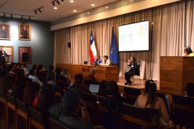 Vista del Salón Domeyko, con gente exponiendo y asistentes eschando. Además, se ve a la intérprete de señas.