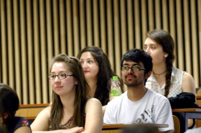 Medio plano de frente de 4 estudiantes sentadas y sentado, prestando atención en una clase.