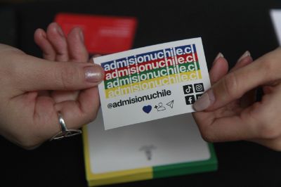 Primer plano de unas manos sosteniendo un stiker de Admisión Uchile