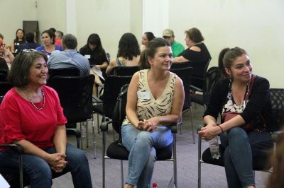 Tres mujeres sentadas en círculo, sonriendo, en la sala Eloísa Díaz. Atrás se ve otro círculo de personas, familiares de estudiantes.