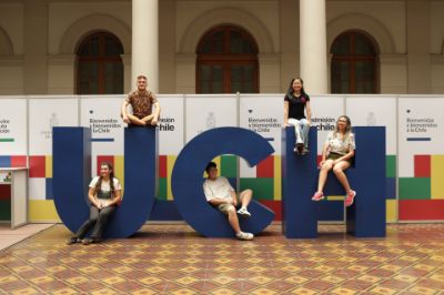 Cinco estudiantes, dos mujeres y tres hombres, posan sentados arriba del volumétrico de las letras UCH, instalado en Casa Central para el proceso de matrícula.
