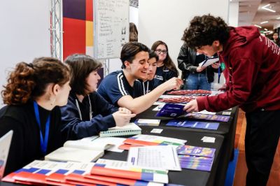 Stand, donde un estudiante conversa con escolar, ambos sonrientes