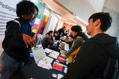 Nairobis, monitora del stand de Pedagogías, conversando con escolar. Al fondo se van más monitores y escolares conversando.