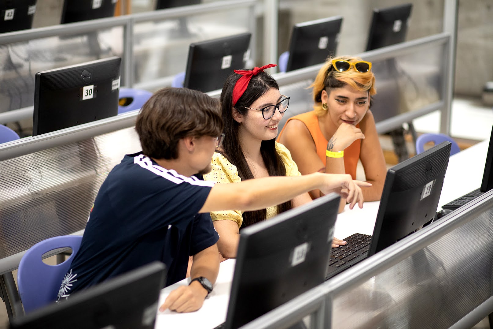 En la foto, tres estudiantes mirando la pantalla de un computador