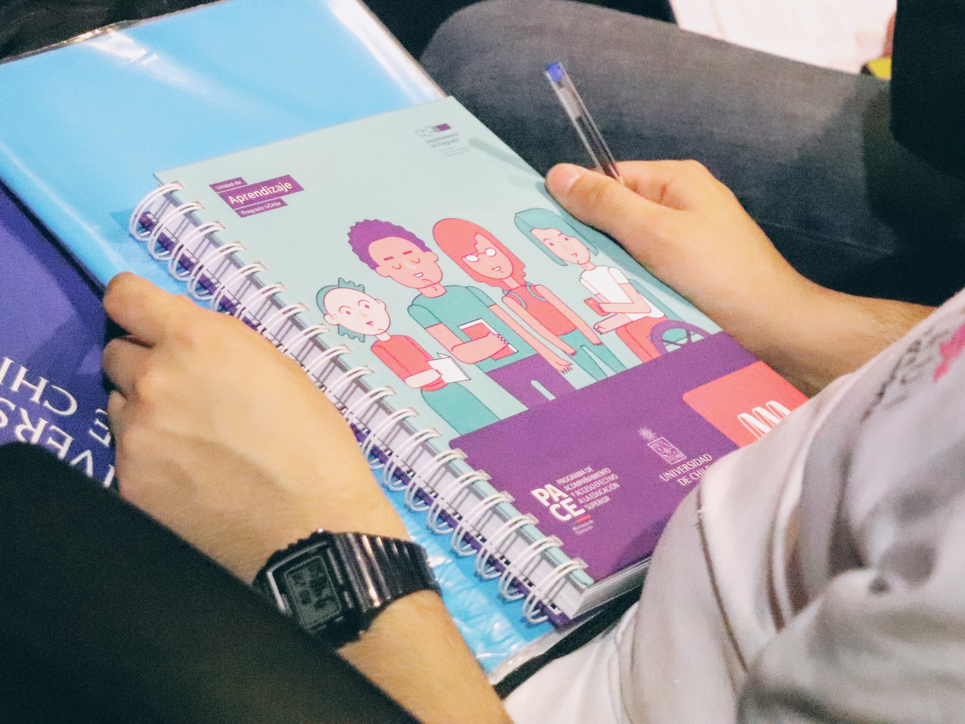En la foto, primer plano a la portada de un cuaderno universitario, en manos de un estudiante